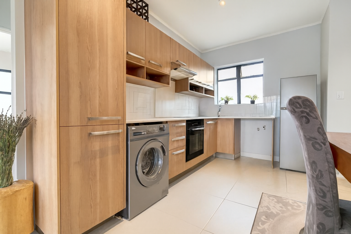 Modern kitchen featuring light wood cabinetry, integrated oven, extractor fan, and tiled flooring with a dedicated space for a washing machine.