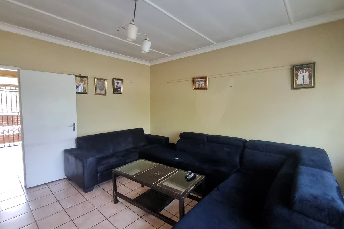 A living room featuring tiled flooring and a ceiling light fixture, with access to an exterior security gate.