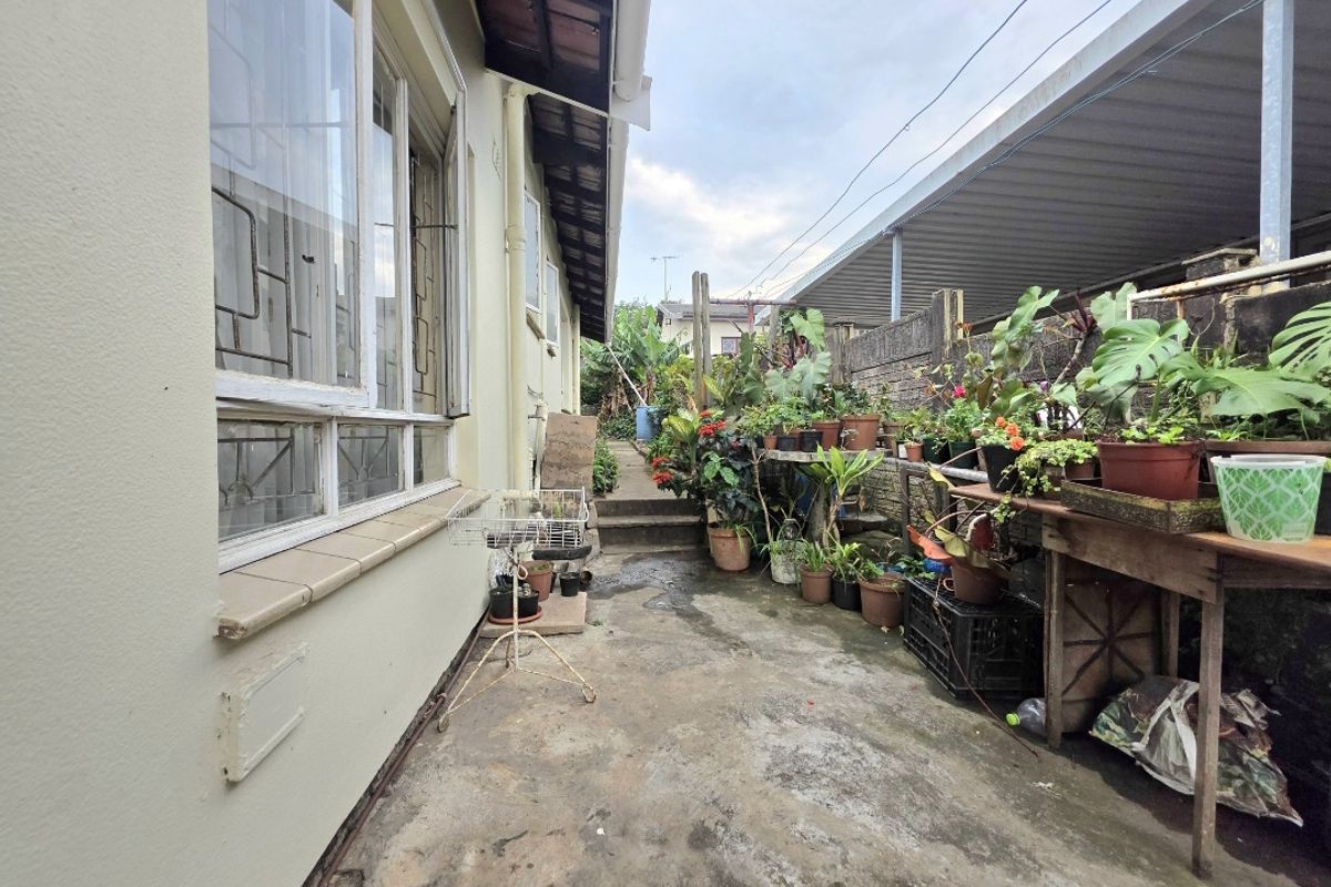 A narrow rear exterior walkway featuring concrete paving, a brick boundary wall, and access to the side of the house.