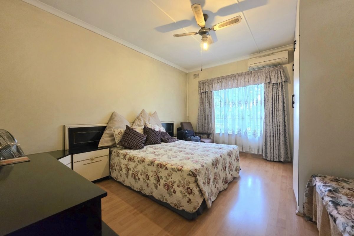 A well-proportioned bedroom featuring laminate flooring, a ceiling fan, and a wall-mounted split-system air conditioner for climate control.
