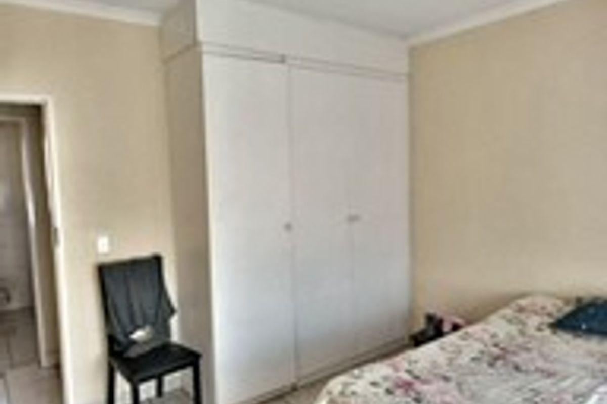 A bedroom featuring built-in floor-to-ceiling cupboards and tiled flooring, with an adjacent doorway leading to an adjoining room.