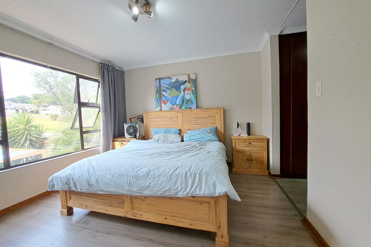 A well-lit bedroom featuring laminate flooring, a large window providing natural light, and a built-in cupboard for storage.