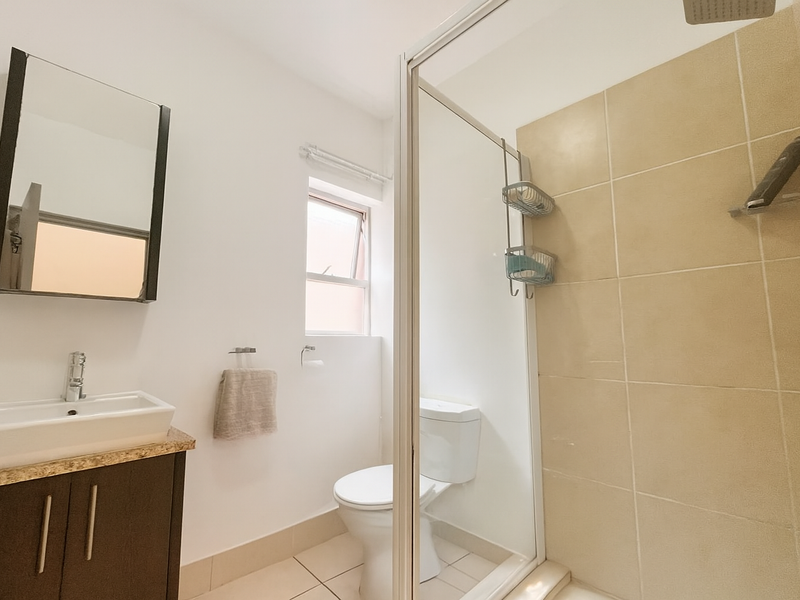 A clean, functional bathroom featuring a modern vanity, toilet, and a glass-enclosed shower with neutral wall tiling.