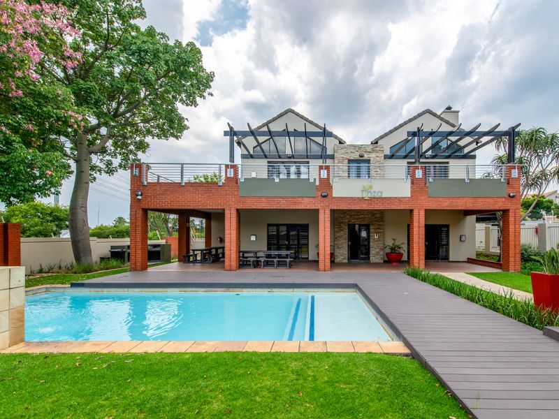 Rear view of the townhouse featuring a swimming pool, timber decking, covered patio area with built-in braai, and an upper-level balcony.