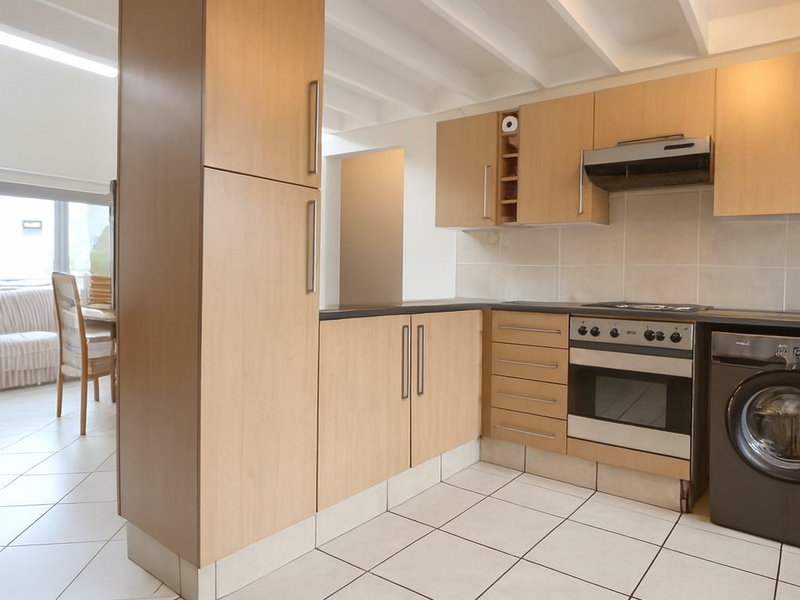 A functional kitchen featuring light wood cabinetry, built-in oven, extractor fan, and ceramic tile flooring, with an open-plan layout connecting to the dining area.
