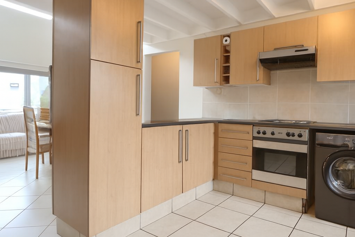A functional kitchen featuring light wood cabinetry, built-in oven, extractor fan, and ceramic tile flooring, with an open-plan layout connecting to the dining area.