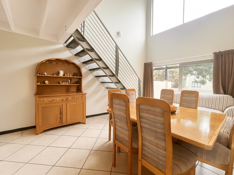Spacious living area featuring double volume ceilings, large windows for natural light, tiled flooring, and a modern metal staircase leading to the upper level.