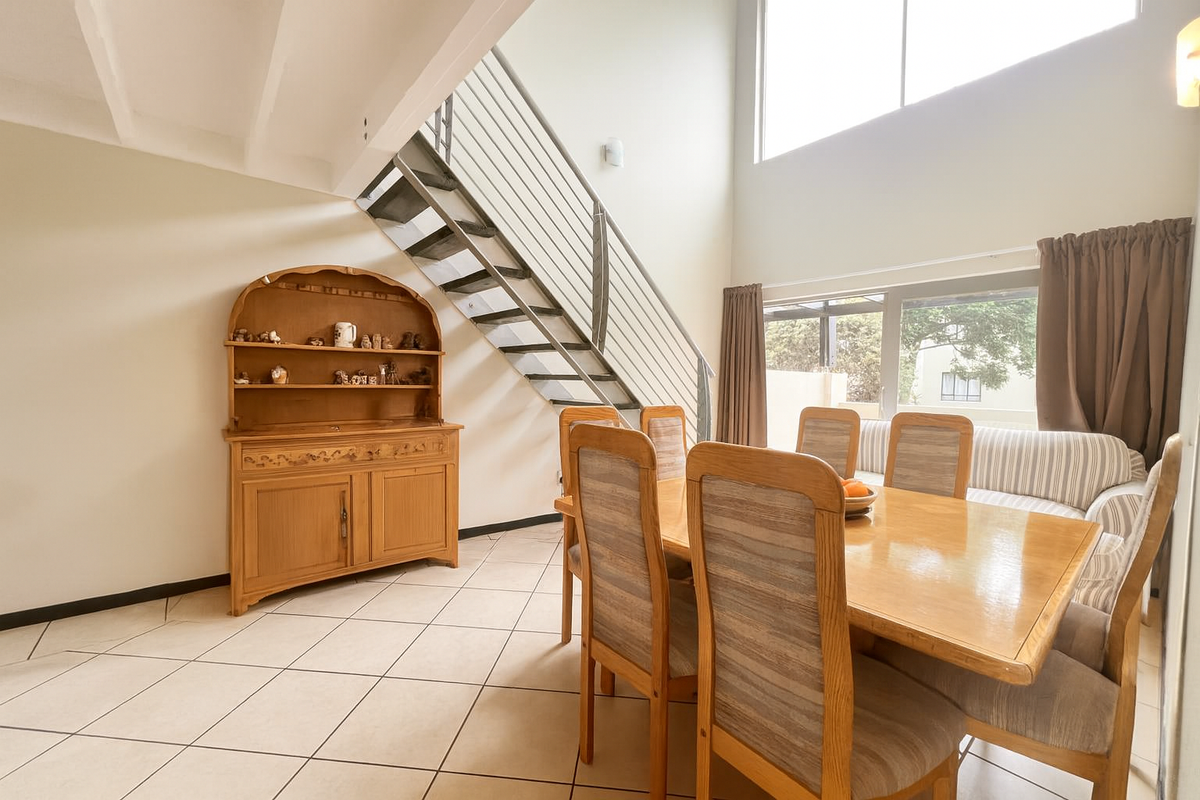 Spacious living area featuring double volume ceilings, large windows for natural light, tiled flooring, and a modern metal staircase leading to the upper level.