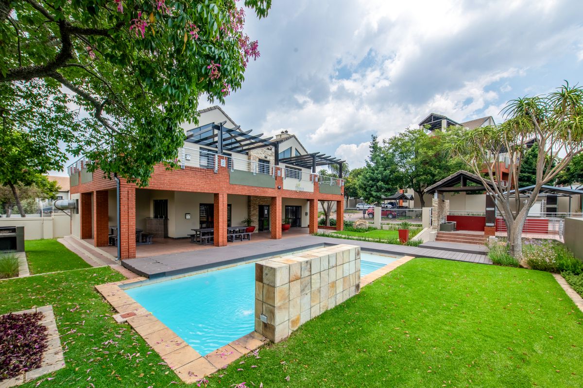 Spacious rear exterior featuring a swimming pool with a stone feature wall, a covered patio with brick pillars, and a well-maintained landscaped garden.