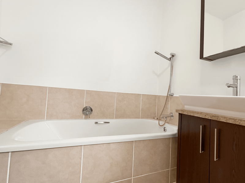 A clean, functional bathroom featuring a built-in bathtub with tiled surround, a modern vessel sink on a dark wood vanity, and a wall-mounted mirror.