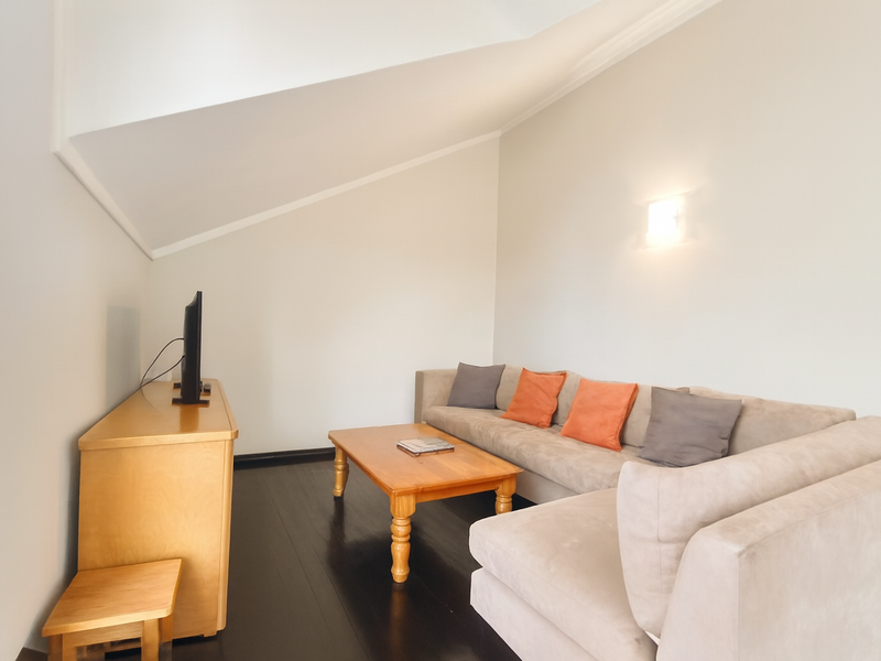 A cozy living room featuring a sloped ceiling, dark timber flooring, and a wall-mounted light fixture, creating a comfortable and inviting atmosphere.