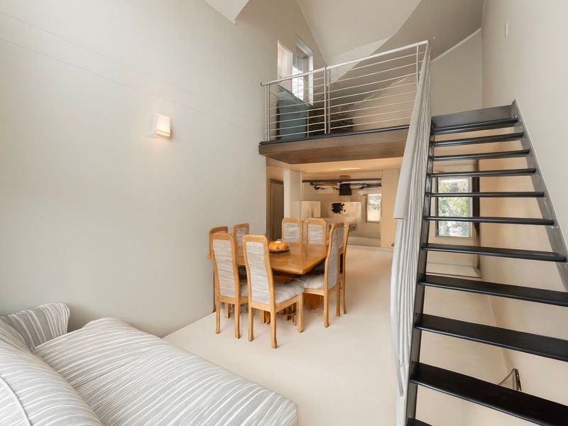 Open plan living area featuring a mezzanine level, vaulted ceilings, and a modern metal staircase with stainless steel balustrades.