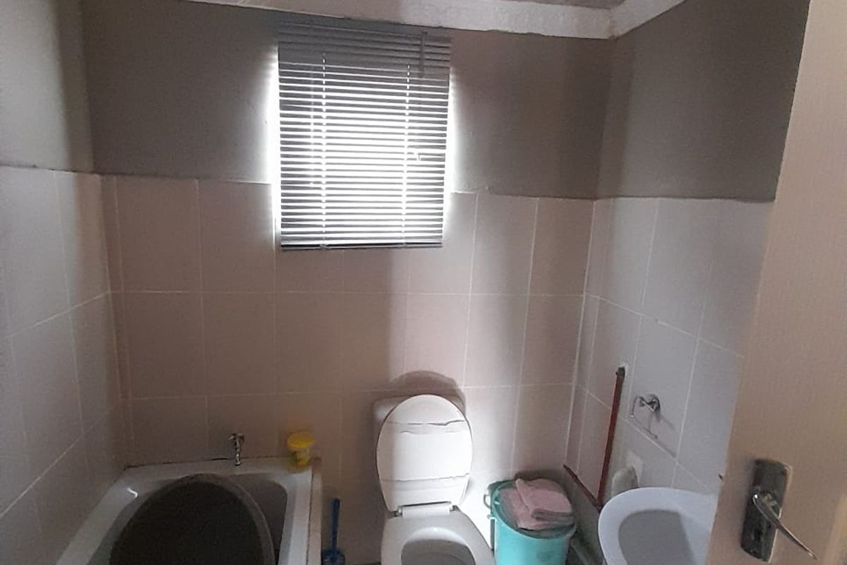 A compact bathroom featuring a bathtub, pedestal basin, and toilet, with tiled finishes and a textured ceiling, requiring cosmetic updates.