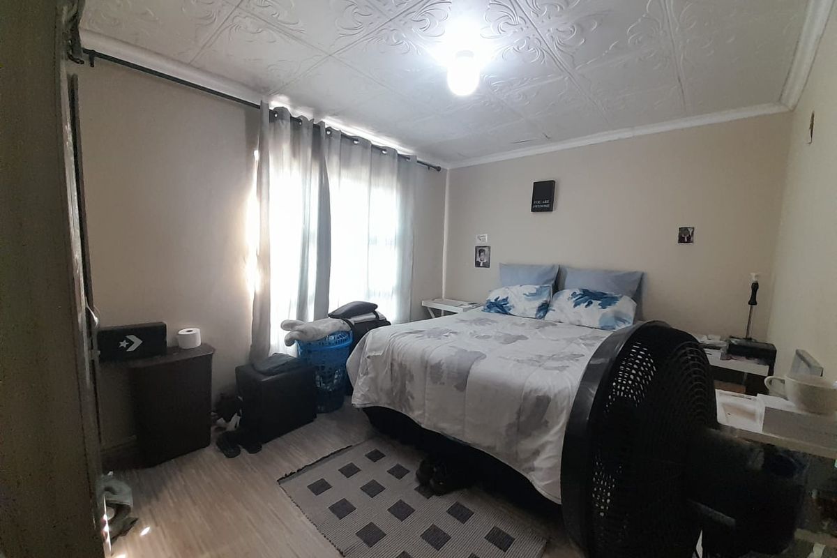 A bedroom featuring a decorative pressed metal ceiling and light-toned laminate flooring, offering a functional space with natural light.