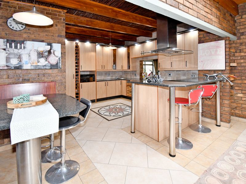 Spacious open-plan kitchen featuring exposed timber beams, brick walls, granite countertops, and a breakfast bar, creating a warm and rustic atmosphere.
