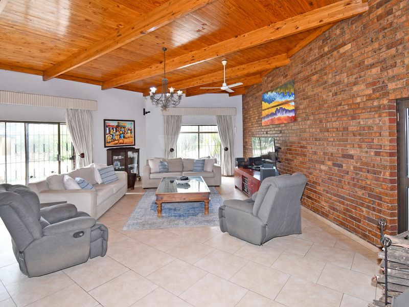 Spacious living room featuring an exposed timber beam ceiling, a large exposed brick feature wall, tiled flooring, and sliding glass doors to the exterior.