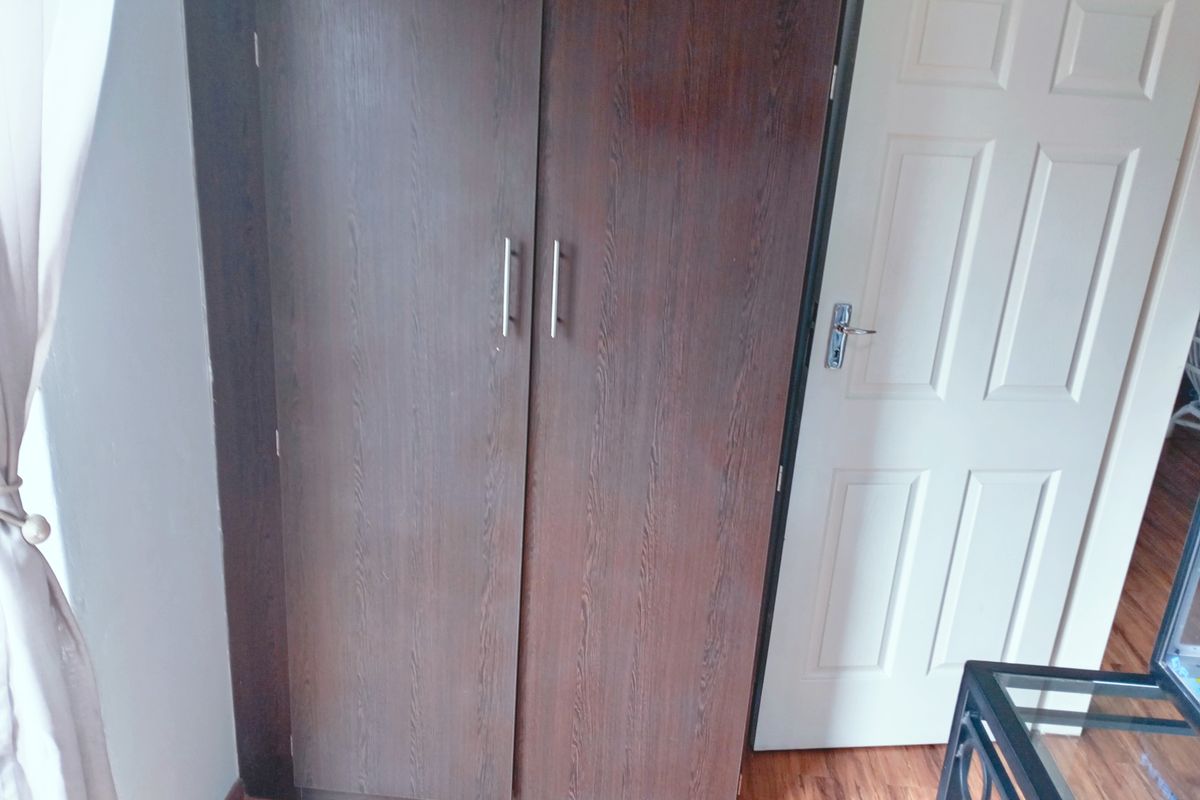 A bedroom interior featuring a dark wood-finish built-in wardrobe and a classic white panel door with laminate flooring.