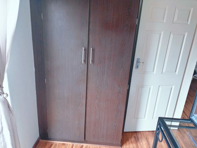 A bedroom interior featuring a dark wood-finish built-in wardrobe and a classic white panel door with laminate flooring.