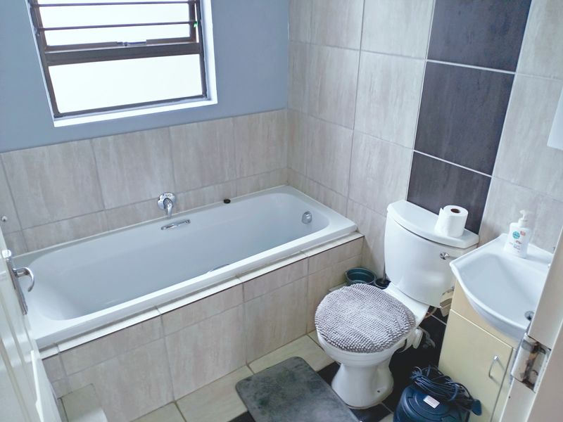 A functional bathroom featuring a built-in bathtub, toilet, and vanity basin with neutral wall and floor tiling.