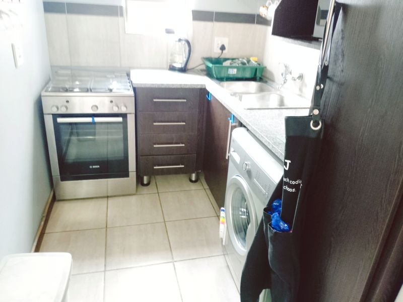 Compact scullery area featuring a stainless steel gas stove, built-in oven, granite countertops, and double bowl sink with tiled finishes.