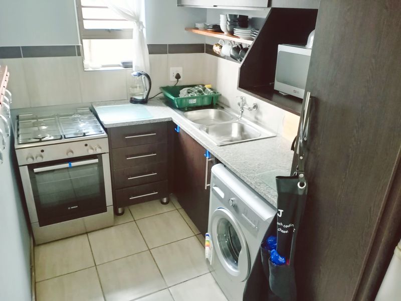 Compact kitchen featuring dark laminate cabinetry, granite countertops, a gas stove with oven, and integrated space for a washing machine.