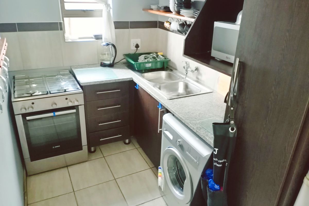 Compact kitchen featuring dark laminate cabinetry, granite countertops, a gas stove with oven, and integrated space for a washing machine.