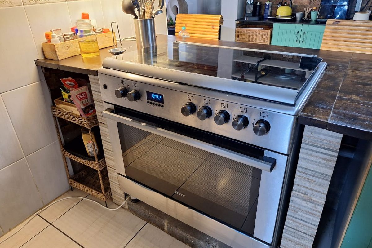A kitchen area featuring a built-in stainless steel oven and hob unit with tiled splashbacks and dark wooden countertops.