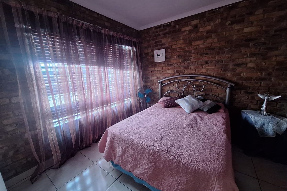 A bedroom featuring exposed brick walls, tiled flooring, and a large window with fitted blinds.