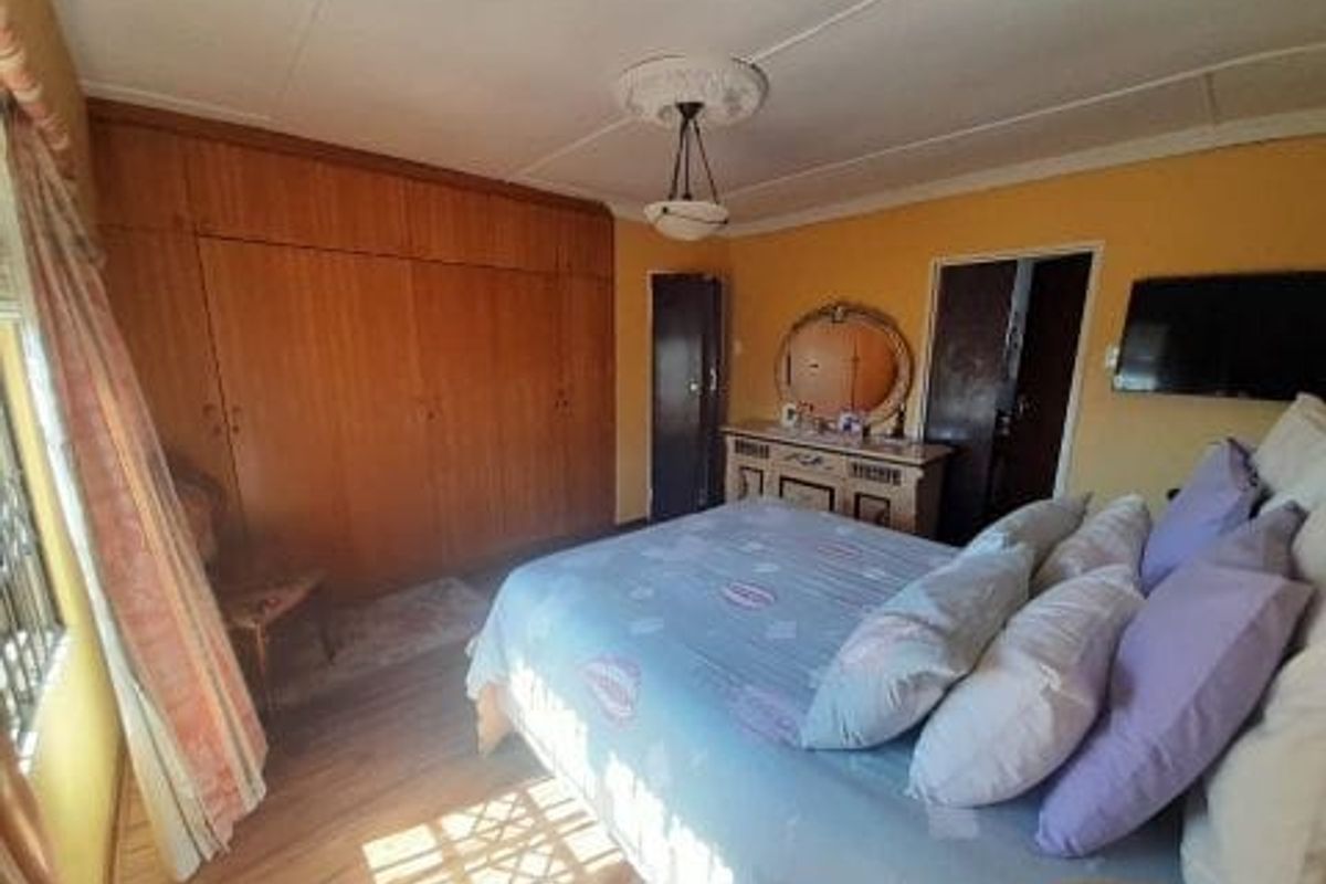 A bedroom featuring built-in wooden cupboards, laminate flooring, and a ceiling rose, requiring cosmetic updates to modernize the space.