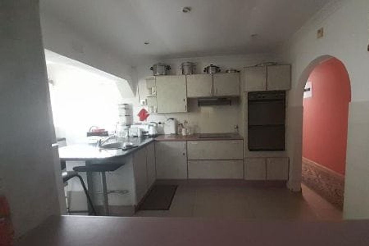 A functional kitchen featuring built-in cabinetry, a double wall oven, an extractor fan, and a breakfast bar, connected to the home via an archway.