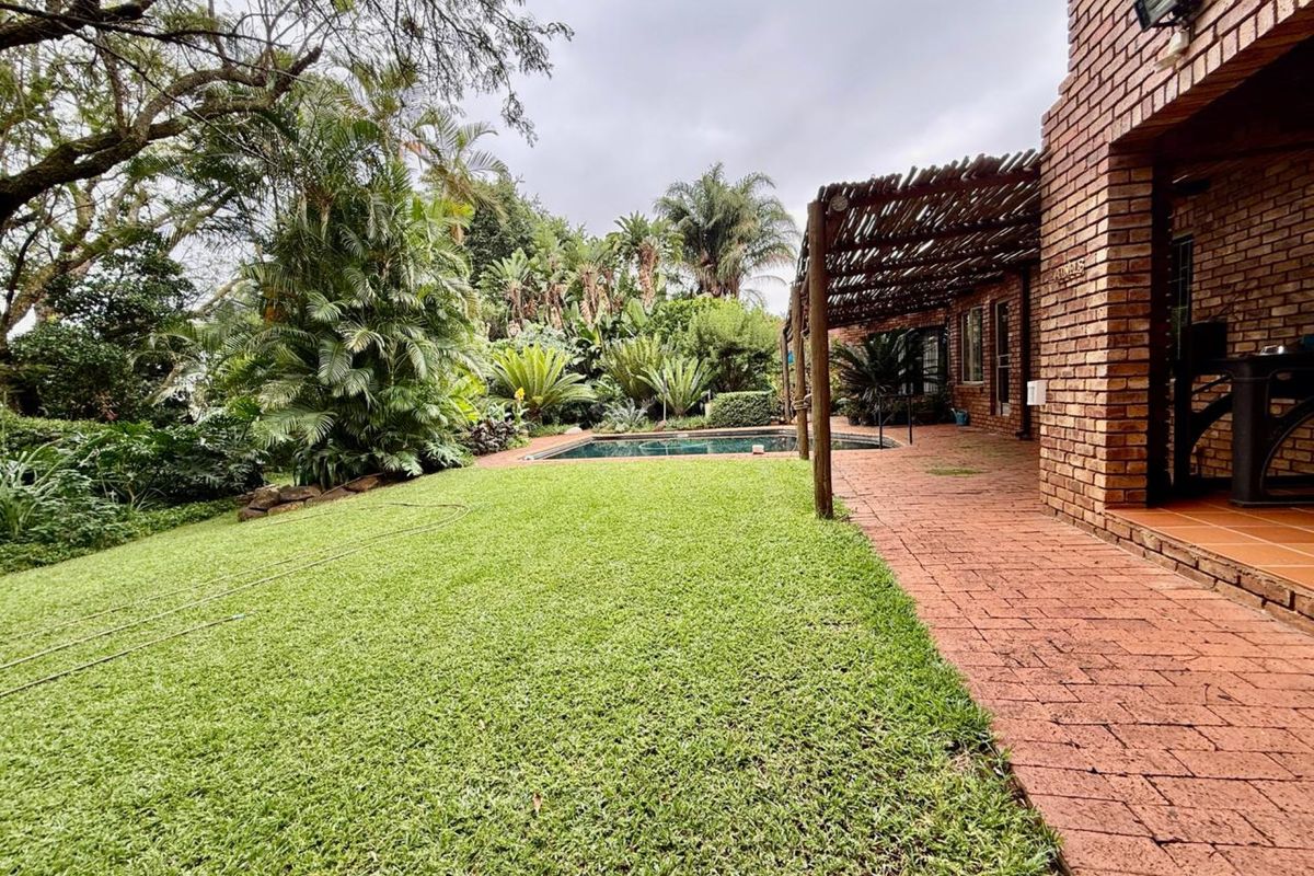 A spacious rear garden featuring a swimming pool, lush landscaping, and a covered brick patio area with a rustic timber pergola.