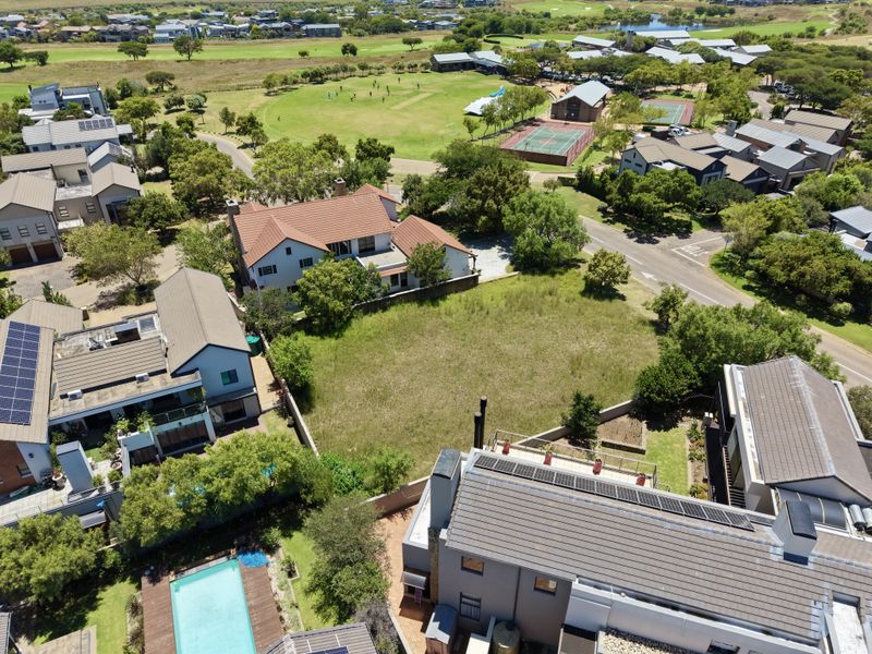 Aerial view of a vacant residential plot situated within a developed estate, featuring surrounding homes and nearby community sports facilities.