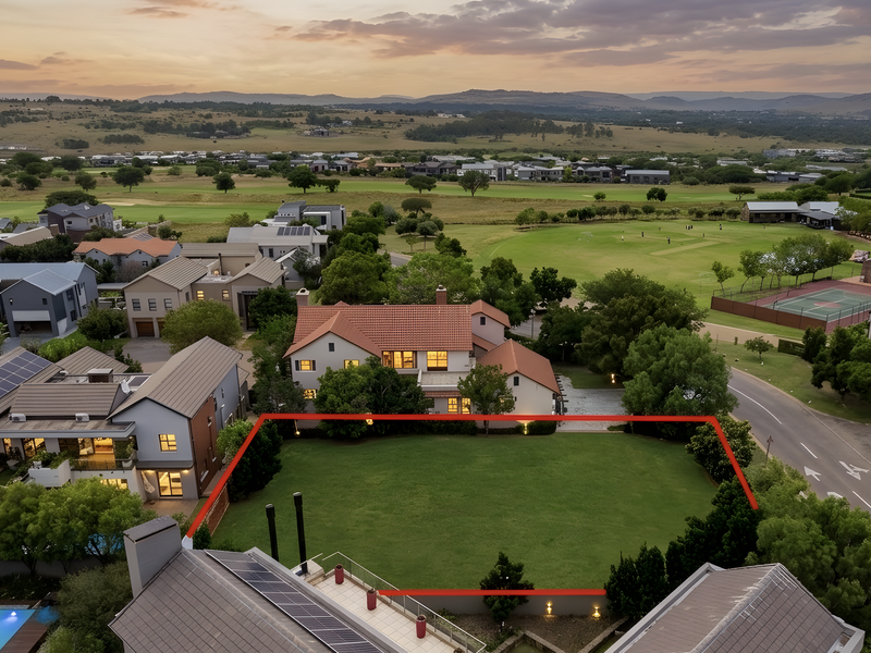 An aerial view of a vacant residential plot featuring a well-maintained lawn, perimeter wall, and exterior lighting within a secure estate setting.