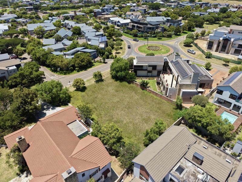 An aerial view of a vacant residential plot situated within a developed suburban estate, surrounded by established homes and infrastructure.