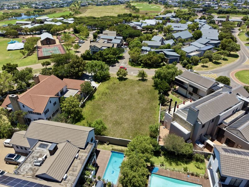 An aerial view of a vacant residential plot situated within a developed estate, surrounded by established homes and community amenities.