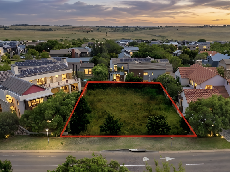 An aerial view of a vacant residential plot situated within an established estate, featuring clear boundaries and surrounding modern residential homes.