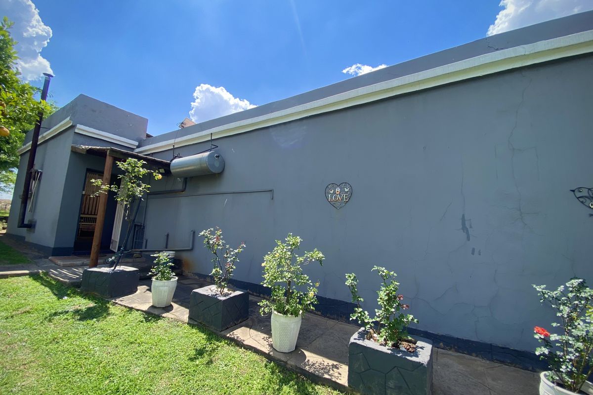 Rear exterior view of the property featuring a grey plastered wall, solar geyser installation, and a paved garden walkway.