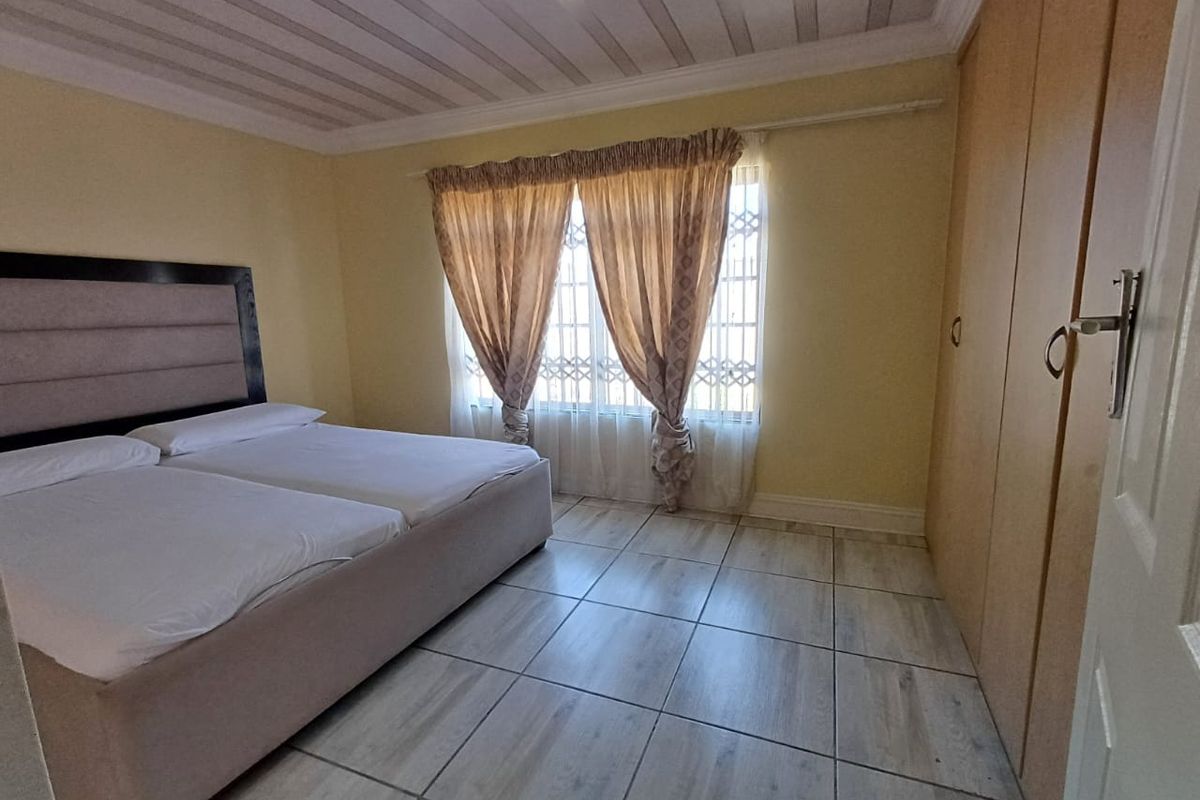 A bedroom featuring tiled flooring, built-in cupboards, and a window fitted with a security gate.