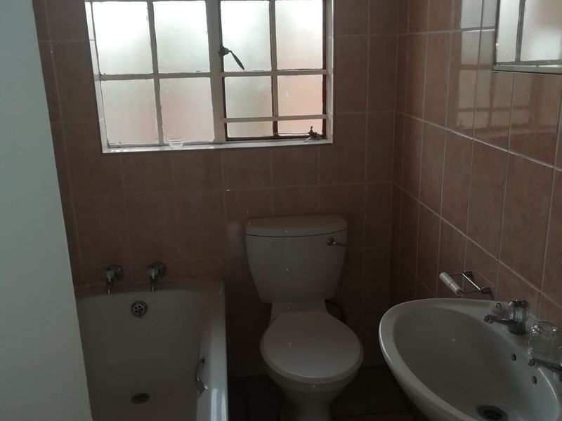 A functional bathroom featuring a bathtub, pedestal basin, and toilet with neutral wall and floor tiling.
