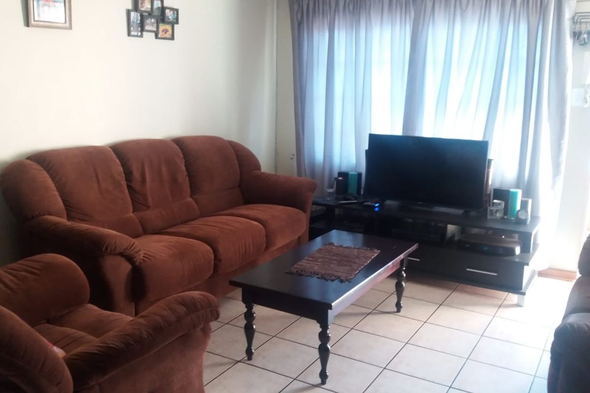 A living room featuring tiled flooring and large windows with curtains, providing a functional and comfortable space for relaxation.