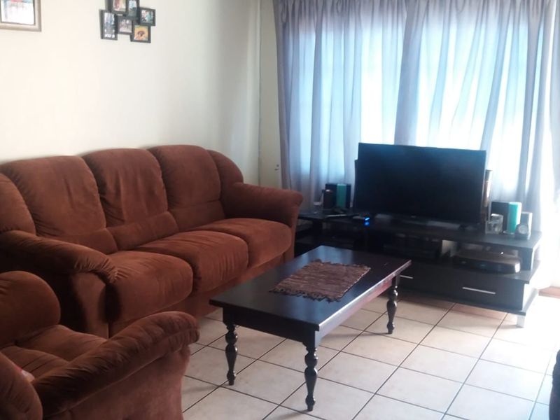 A living room featuring tiled flooring and large windows with curtains, providing a functional and comfortable space for relaxation.