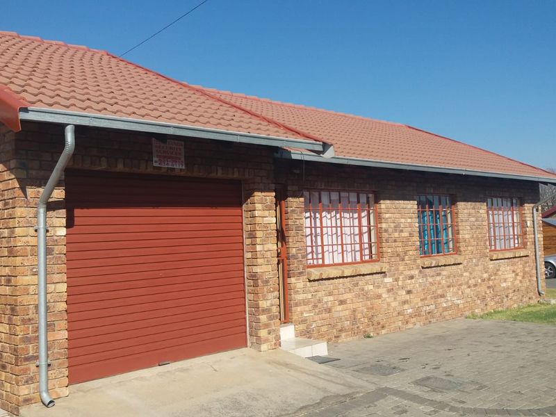 Front elevation of a face brick house featuring a roller garage door, tiled roof, and security bars on the windows with a paved driveway.