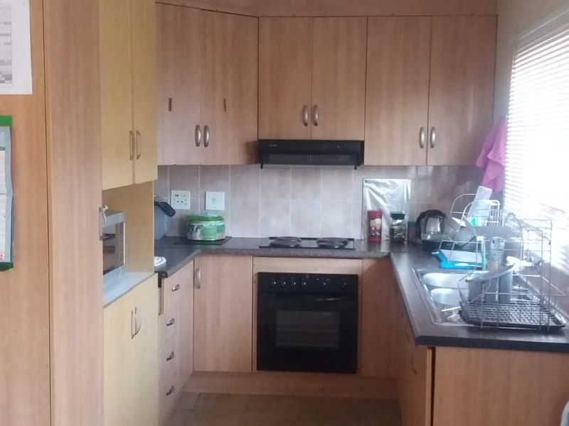 A functional kitchen featuring laminate cabinetry, built-in oven, electric hob, extractor fan, and a double bowl sink with tiled splashback.