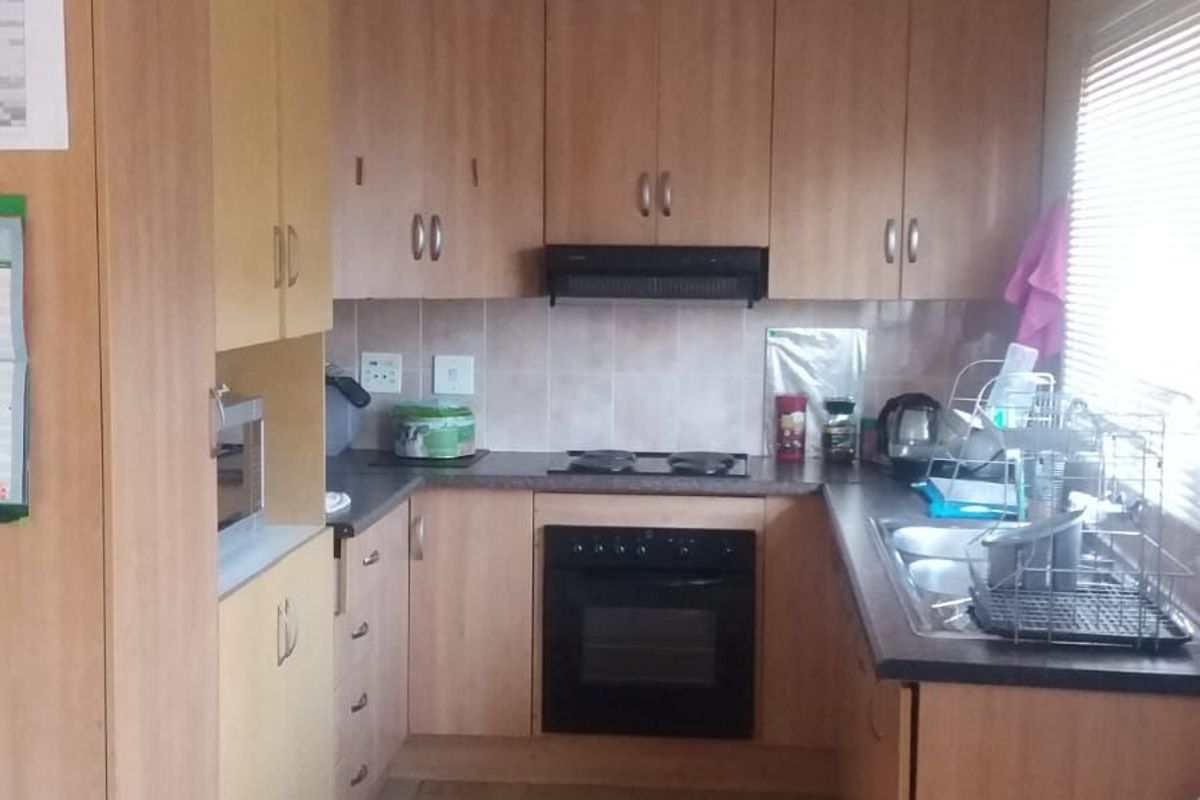 A functional kitchen featuring laminate cabinetry, built-in oven, electric hob, extractor fan, and a double bowl sink with tiled splashback.