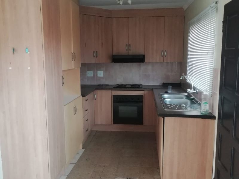 A functional kitchen featuring laminate cabinetry, built-in oven, hob, extractor fan, and a double bowl sink, requiring some cosmetic updates to the flooring and finishes.