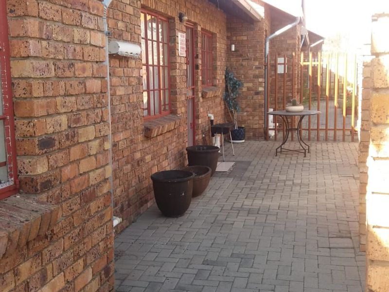 A side exterior view of the property featuring face brick walls, a paved walkway, and secure metal gate access.