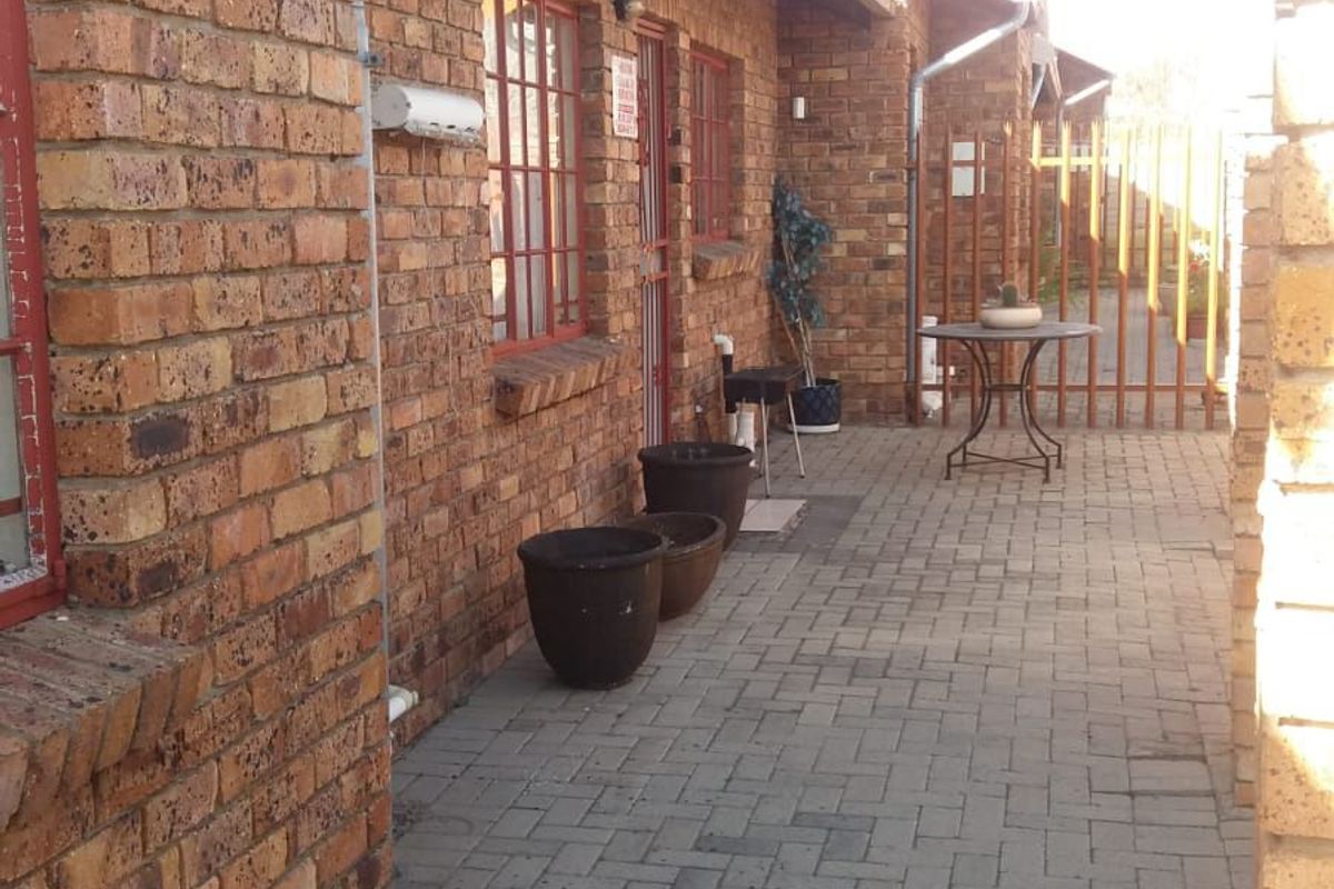 A side exterior view of the property featuring face brick walls, a paved walkway, and secure metal gate access.