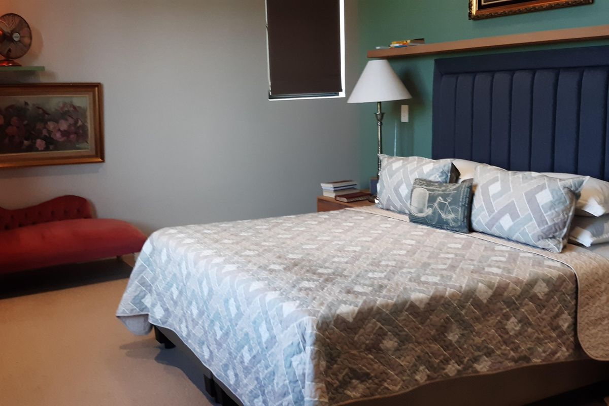 A well-maintained bedroom featuring a large built-in headboard with an integrated floating shelf and neutral wall finishes.