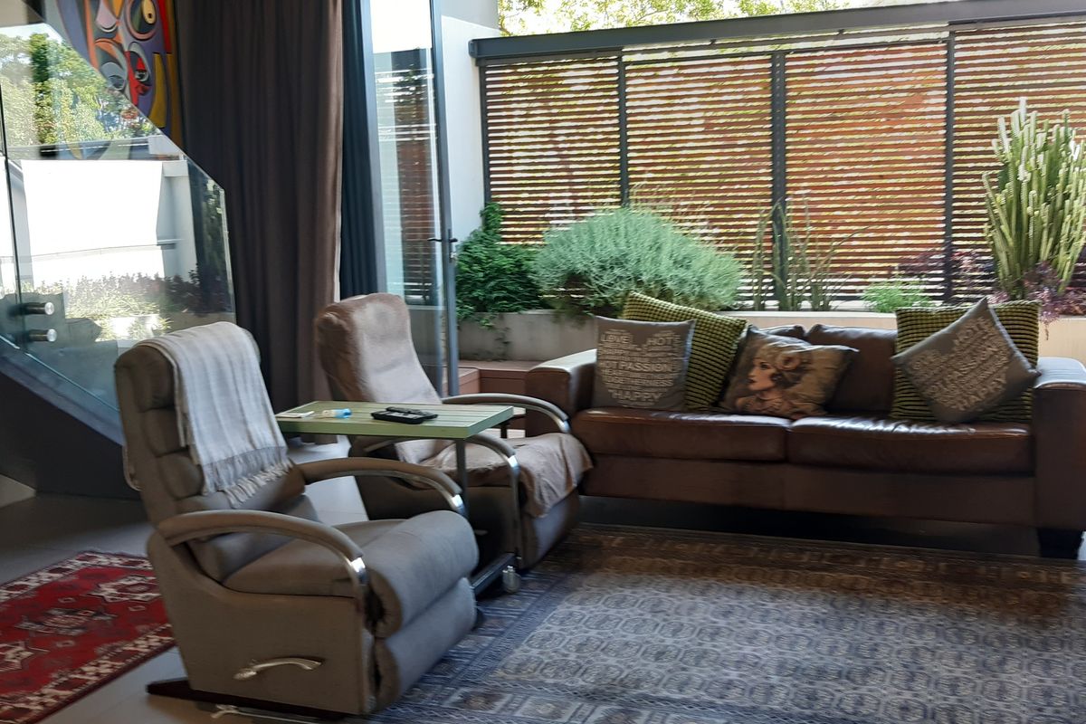 A modern living room featuring a glass balustrade staircase, large sliding doors opening to a private outdoor area with timber screening.