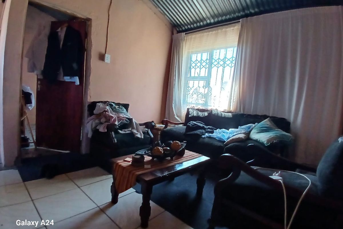 A living room featuring tiled floors and a corrugated metal ceiling, requiring cosmetic updates and repairs to wall finishes and electrical fixtures.